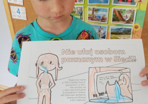 Chłopiec z grupy Słoneczka prezentuje pracę plastyczną o tym aby nie ufać osobom poznanym w sieci.