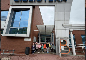 Zdjęcie przedstawia grupę Smerfów, która pozuje pod budynkiem Biblioteki