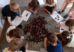 Dzieci układają tyle kasztanów na kartce ile wskazuje cyfra.