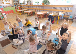 Dzieci siedzą przed dywanikami i podnoszą do góry 2 kasztany.