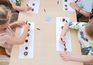 Dzieci ćwiczą grafomotorykę z użyciem kasztanów.