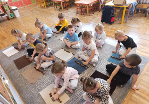 Dzieci siedzą przed dywanikami i przeliczają kasztany.