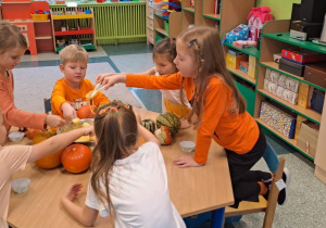 Dzieci siedzą przy stoliku i nakładają łyżkami ciasto do foremek.