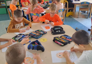 Dzieci siedzą przy stolikach i wykonują pracę plastyczną dynię.