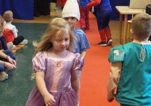 Dzieci w bajkowych strojach idą po czerwonym dywanie w pokazie mody.