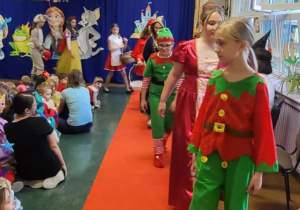 Dziewczynki przebrane za Skrzaty, Kopciuszka, Królewnę Śnieżkę, Królika, Wróżkę idą po czerwonym dywanie.