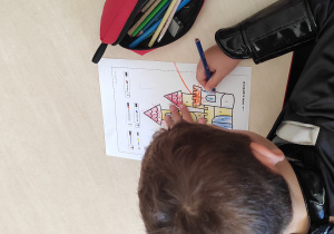 Chłopiec siedzący przy stoliku koloruje ilustrację bajkowego zamku.