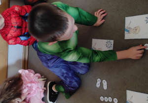 Chłopiec układa liczmany- płatki śniegu obok ilustracji przedstawiającej Elzę, zgodnie z podanym na ilustracji działaniem.