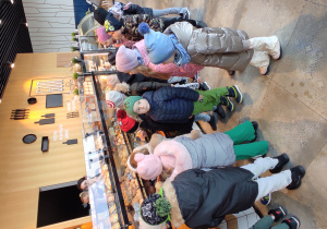 Dzieci ustawione w kolejce przyglądają się produktom, które można kupić w sklepie.