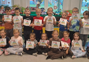 Dzieci pozują do zdjęcia grupowego ze swoimi pracami.