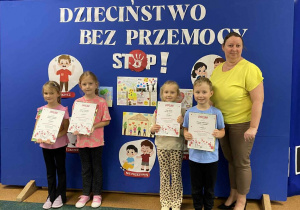 Dzieci biorące udział w konkursie plastycznym Dzieciństwo Bez Przemocy pozują do zajęcia z wicedyrektor, trzymając otrzymane nagrody.