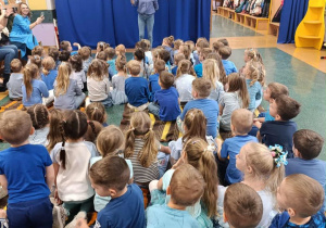 Dzieci z grup trzylatków, czterolatków oraz pięciolatków, ubrane na niebiesko słuchają pogadanki przeprowadzonej przez pedagoga specjalnego.