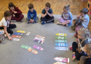 Dzieci siedzą na dywanie, dziewczynka układa kredki wg kodu.