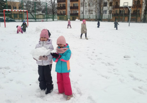 Dwie dziewczynki pozują do zdjęcia trzymając kule śnieżne w rękach.