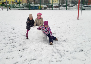 Dziewczynki stoją przy dużej śniegowej kuli.