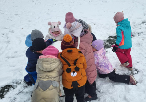 Dzieci toczą ogromną śniegową kulę.