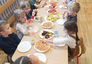 Dzieci siedzą wspólnie przy stole i mają słodki poczęstunek.