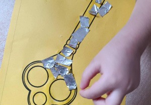 Dziewczynka wykleja obrazek klucza sreberkiem.