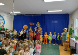 Zdjęcie przedstawia dzieci z grupy Odkrywcy przygotowane do występu, a nauczycielka zapowiada występ.