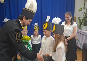 Dziewczynka wraz z chłopcem z grupy Motylki w ramach podziękowań za przybycie do naszego przedszkola wręczają panu górnikowi własnoręcznie wykonaną laurkę z życzeniami oraz bukiet kwiatów z krepiny.