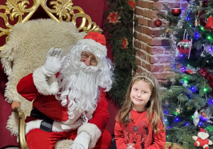 Dziewczynka pozuje do zdjęcia ze Świętym Mikołajem.