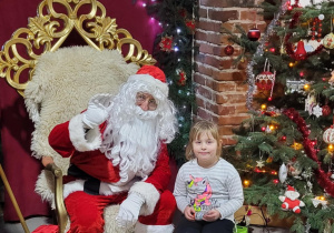 Dziewczynka pozuje do zdjęcia ze Świętym Mikołajem.