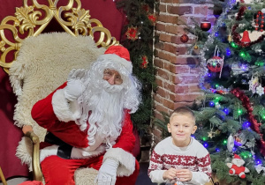 Chłopiec pozuje do zdjęcia ze Świętym Mikołajem.