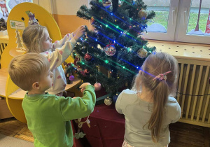 Dzieci zawieszają świąteczne ozdoby na choince.
