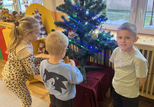 Dzieci zawieszają świąteczne ozdoby na choince.