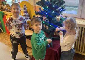 Dzieci zawieszają świąteczne ozdoby na choince.
