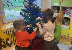 Dzieci zawieszają świąteczne ozdoby na choince.