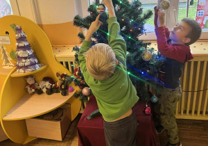 Chłopcy zawieszają świąteczne ozdoby na choince.