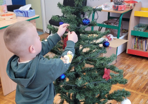 Chłopiec wiesza bombkę na choince.