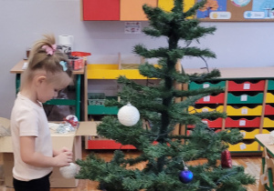 Dziewczynka wiesza bombkę na choince.