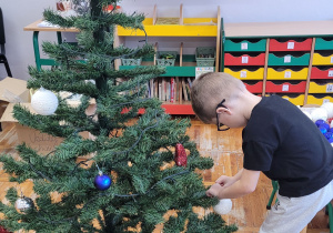 Chłopiec wiesza bombkę na choince.