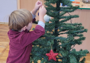 Chłopiec wiesza bombkę na choince.