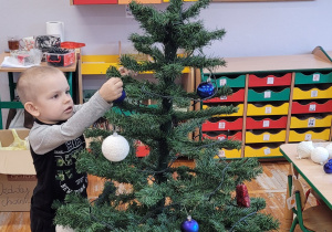 Chłopiec wiesza bombkę na choince.