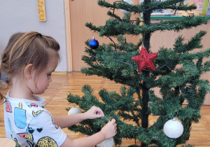 Chłopiec wiesza bombkę na choince.
