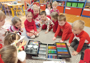 Dzieci siedzą na dywanie i oglądają prezent od Mikołaja.