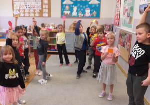 Zdjęcie przedstawia dzieci bawiące się w zabawę ruchową z figurami geometrycznymi.