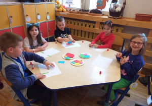 Zdjęcie przedstawia dzieci bawiące się w zabawę ruchową z figurami geometrycznymi.