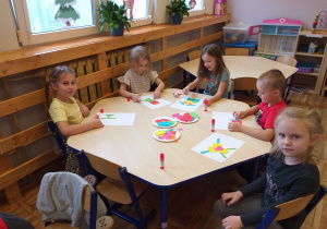 Zdjęcie przedstawia dzieci bawiące się w zabawę ruchową z figurami geometrycznymi.