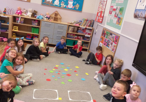 Zdjęcie przedstawia dzieci przed segregowaniem figur geometrycznych ze względu na kolor.