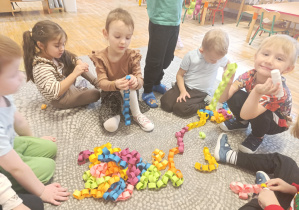 Dzieci siedzą na dywanie i sklejają papierowy łańcuch
