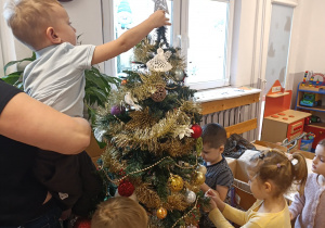 Chłopiec zakłada gwiazdkę na czubek drzewka