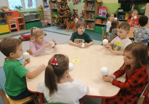 Dzieci siedzą przy stole na stole przygotowane są bombki styropianowe i serwetki.
