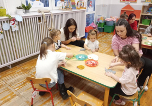 Dwie mamy z dziećmi dekorują ozdoby na choinkę.