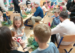 Zdjęcie przedstawia dzieci wraz z ich rodzicami wykonującymi stroik świąteczny.