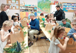 Zdjęcie przedstawia dzieci wraz z ich rodzicami wykonującymi stroik świąteczny.