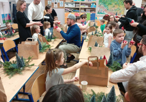 Zdjęcie przedstawia dzieci wraz z ich rodzicami wykonującymi stroik świąteczny.